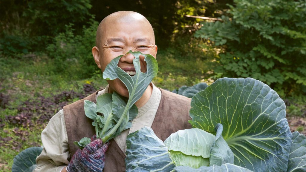 Photo of a Korean nun, Venerable Jeongkwan Snim, smiling with freshly picked cabbages from her temple garden.